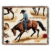 Cream fringed woven blanket featuring a cowboy riding a brown horse, Western hats, flowers, and the words “He Had Me at Darlin’.”