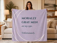 Woman holding a lavender sweatshirt blanket featuring the quote "Morally Gray Men Are My Type. Unfortunately." Cozy reading blanket for fans of dark romance books, romantasy novels, and morally gray heroes.