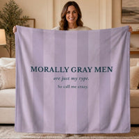 A woman isstanding and holding a  lavender and light gray striped blanket in a living room setting. The blanket features the text 'MORALLY GRAY MEN are just my type. So call me crazy.