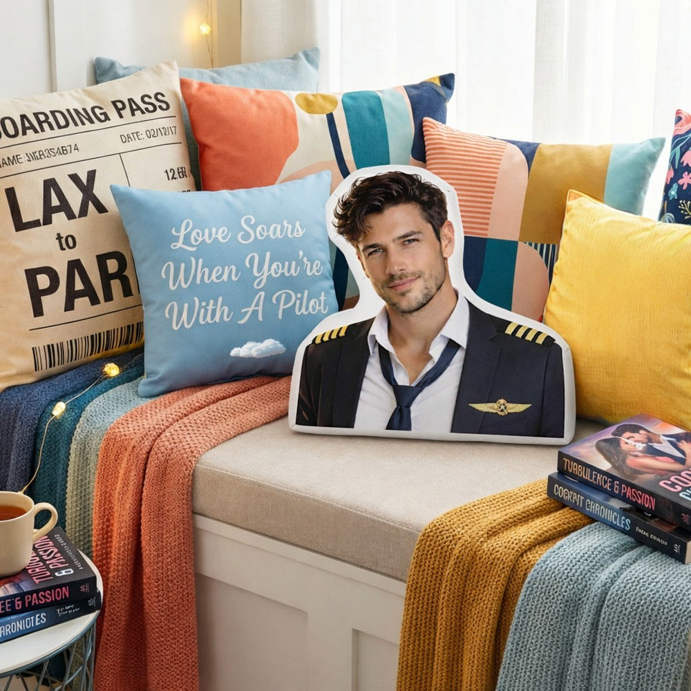 The Pilot aviation romance book boyfriend pillow styled in a cozy reading nook with colorful accent pillows, travel-inspired décor, stacked romance novels, and soft layered throws. The scene features a feminine, inviting space designed for women who love pilot romance, airport reunions, and jet-setting book boyfriends.