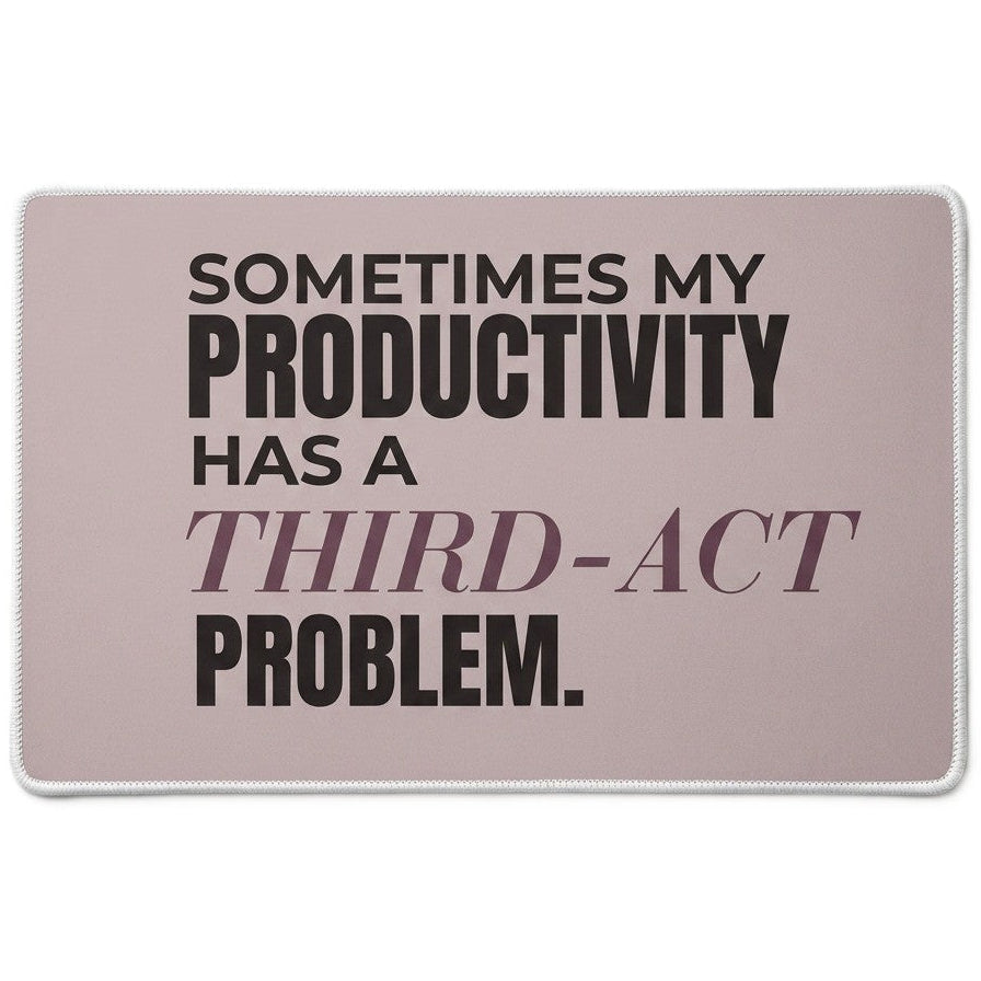 A rectangular desk mat  featuring the humorous quote 'SOMETIMES MY PRODUCTIVITY HAS A THIRD-ACT PROBLEM.' in black and muted plum-colored text on a taupe background.