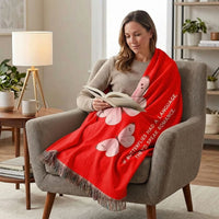 A woman sits in an armchair reading a book, wrapped in a bright red throw blanket featuring pink butterflies and white text that reads, 'IF BUTTERFLIES HAVE A LANGUAGE, THEY'D SPEAK RROMANCE.' 