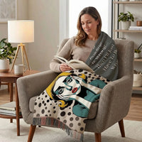 A woman sits in an armchair in a living room, reading a book while draped over her lap is a throw blanket featuring a stylized pop-art face illustration and the quote, 'If reading is wrong, then I'll just have to be wrong.'.