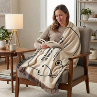 A woman sits in an armchair reading a book, wrapped in a cream throw blanket with black text and stethoscope graphics. The blanket reads, 'READING IS SELF-CARE' and 'DOCTORS MATTER.