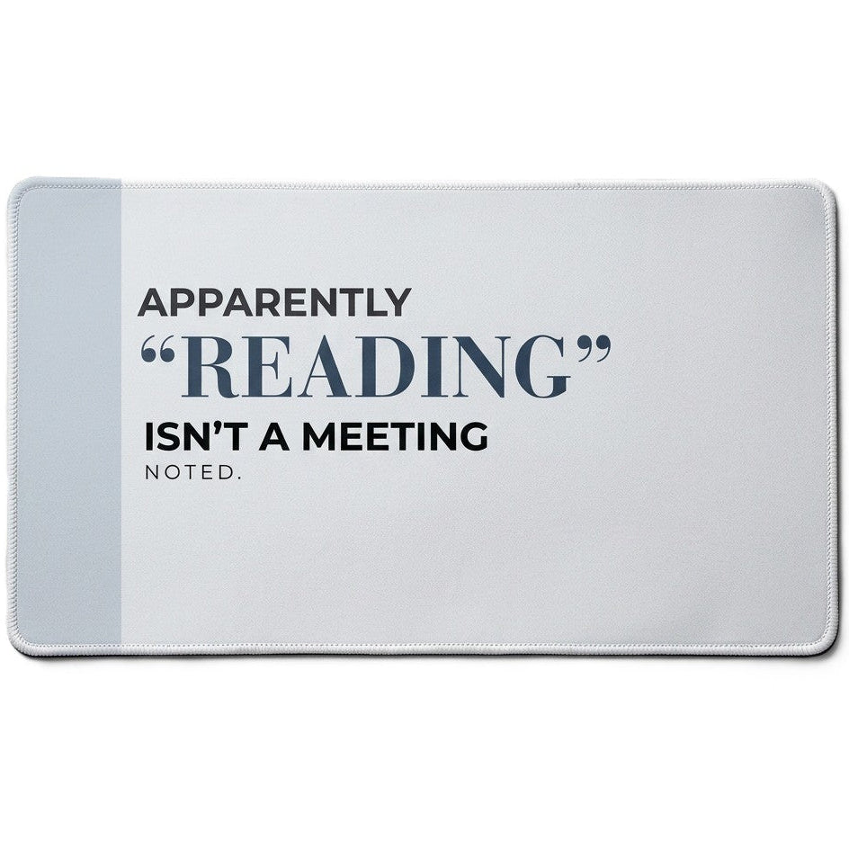 A rectangular desk mat featuring the text 'APPARENTLY "READING" ISN'T A MEETING. NOTED.' in black and navy blue lettering on a light gray background with a darker gray vertical stripe on the left side.