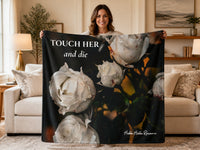 Woman holding a dark floral sweatshirt blanket featuring white roses and the phrase "Touch Her and Die." Romantic gothic-inspired blanket for readers who love possessive heroes, dark romance novels, and romantasy stories.