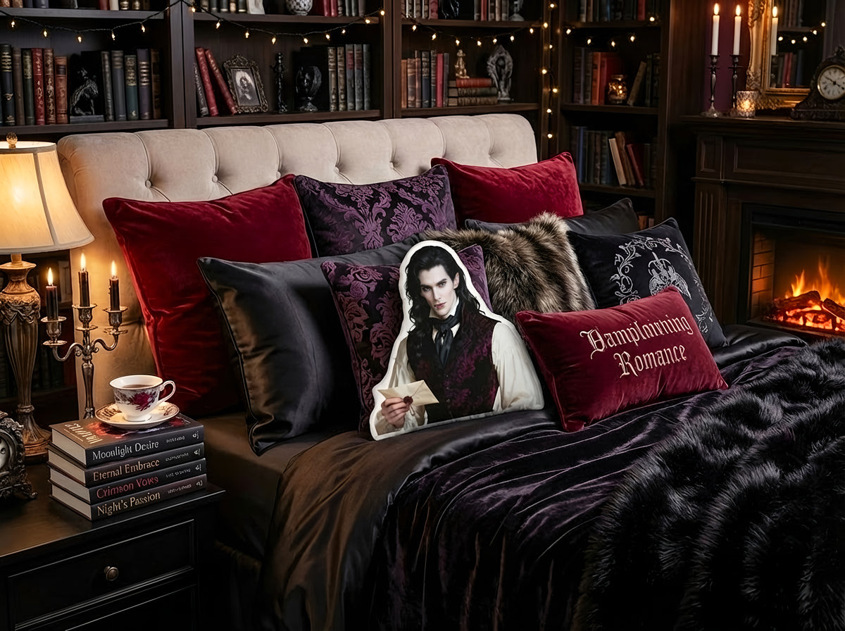 Lifestyle bedroom scene featuring a custom-shaped vampire book boyfriend pillow displayed upright against layered decorative pillows on a bed. The room includes dark wood bookshelves filled with books, warm string lights, black and burgundy velvet pillows, a faux fur accent pillow, and a lit fireplace. The pillow depicts a pale, dark-haired vampire character wearing a patterned vest and holding a sealed letter, styled in a gothic romance aesthetic.